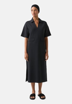Schwarzes, knielanges Kleid mit kragenförmigem Ausschnitt, kurzen Ärmeln und seitlichen Schlitzen. Verfügt über zwei Fronttaschen und einen glatten, strukturierten Stoff.