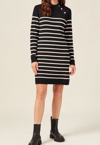 Robe en tricot à manches longues en rayures horizontales noir et crème, avec un col rond orné de boutons et des poignets côtelés.