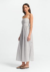 Abito lungo a righe con un corpino aderente in stile bandeau e una gonna fluente. Tessuto leggero in tonalità di grigio e bianco, con spalline sottili.