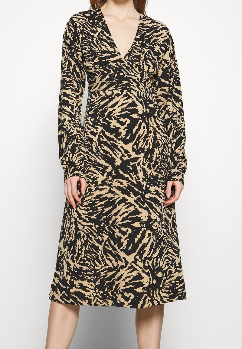 Robe à décolleté profond en V, manches longues et ourlet mi-genou. Présente un imprimé abstrait noir et beige sur un tissu doux.