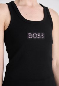 Canottiera nera a coste con logo "BOSS" embellito da cristalli sul davanti. Il collo è a scollo rotondo e le spalline sono larghe.