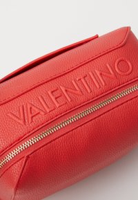 Röd läder toalettväska med ett präglat "Valentino"-logotyp och en guldfärgad dragkedja. Ytan har en strukturerad, grov finish.