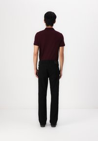 Burgundi pólóing fekete farmernadrággal párosítva, slim fit és egyenes szárajú kialakítással. Minimalista stílus, látható minták vagy díszítések nélkül.