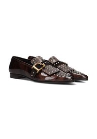 Mocassins en cuir marron foncé avec une finition brillante, présentant un motif clouté et une grande boucle décorative sur la sangle. Semelle plate.
