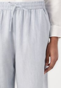 Pantalones de tela a rayas azul claro con cintura elástica y cordón. Cuenta con bolsillos laterales y un corte relajado. Textura suave.