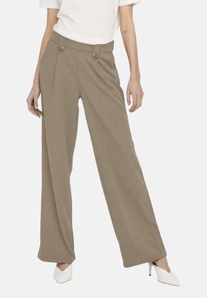 Pantalons beige à jambes larges avec deux boutons à l'avant, design plissé et texture lisse, associés à un top blanc et des talons blancs.