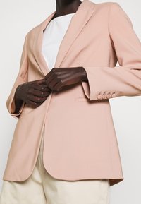 Blazer rosa claro con un corte entallado, solapas con muesca y tres botones en cada puño. Presenta una textura suave y una silueta definida.