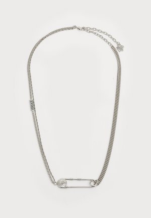 Strieborný náhrdelník s dvoma reťazovými prameňmi, jedným plochým a jedným skrúteným, s veľkou bezpečnostnou ihlou a kruhovým príveskom ako akcentami.