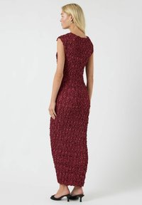 Lilla, tettsittende kjole med et teksturert blomsterpatron, korte ermer og gulvlengde. Minimalistiske svarte hæler kompletterer antrekket.