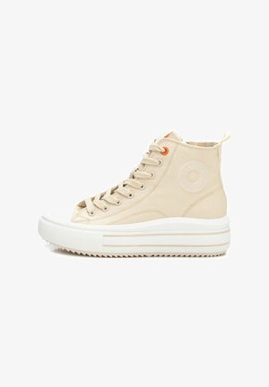 Zapatillas altas de lona beige con punta y suela de goma blanca, que presentan detalles de ojetes naranjas y un acento de logo circular en el lateral.