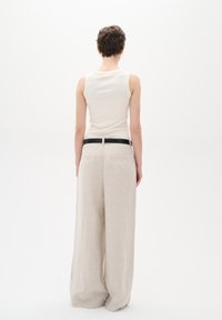 Vitt ribbat linne med rund halsringning, parat med lösa, beige linnebyxor, försedda med ett svart bälte och bakfickor.