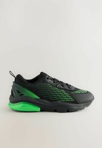 Chaussure de sport noire avec accents verts, tige en mesh, semelle texturée et talon rembourré et brillant en vert. Présente un design à lacets et une languette.