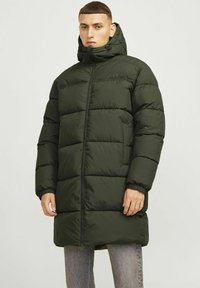 Hřejivá bunda s kapucí v tmavě zelené barvě, vybavená plným zipem a elastickými manžetami. Disponuje prošívanými sekcemi pro izolaci a teplo.
