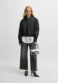 Giacca bomber nera trapuntata, camicia a righe bianche, pantaloni in denim grigio a gamba larga, mules nere con tacco e una borsa argentata con tracolla a catena.