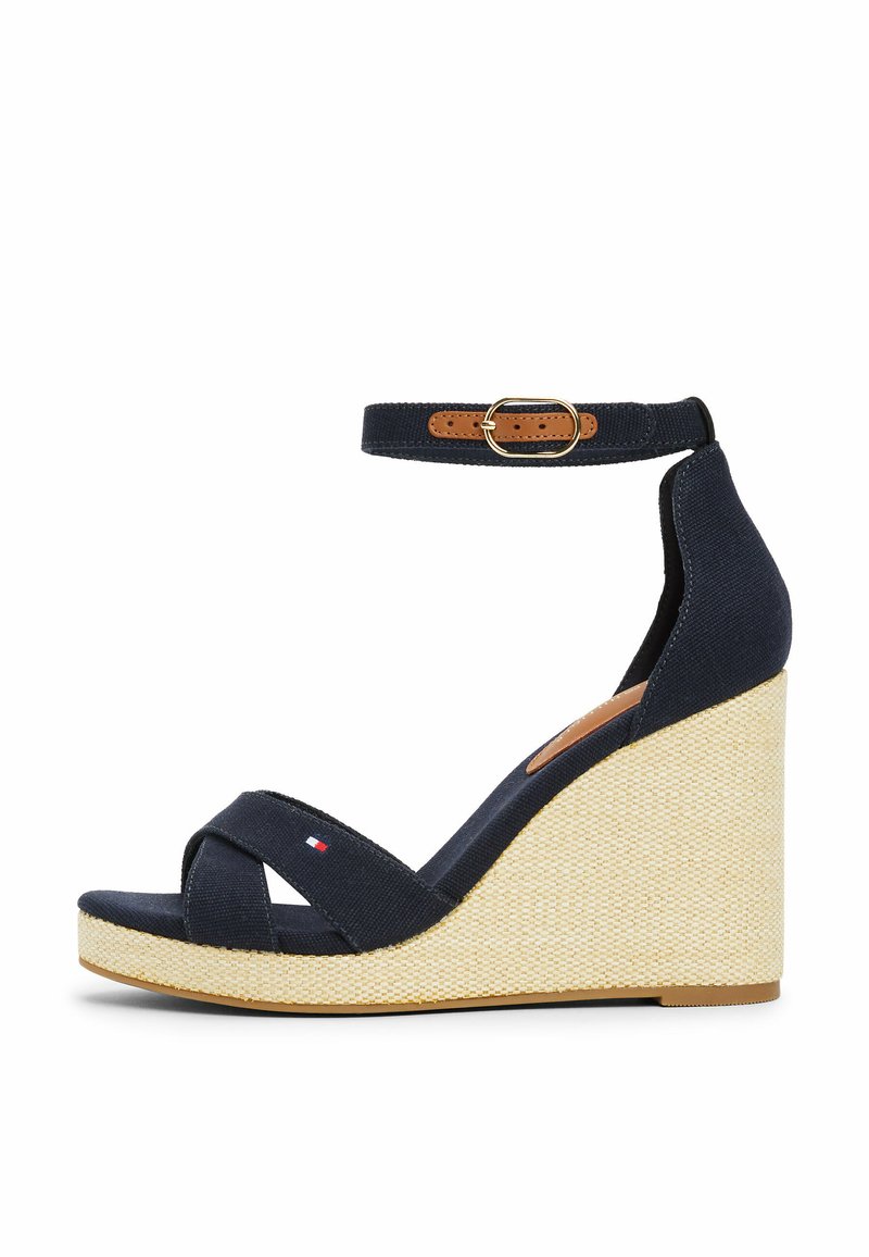 Wedge sandal in dark navy canvas with crossed straps; features a textured beige espadrille-style platform and ankle strap with a gold buckle.