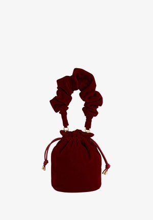 Dieprode fluwelen trekzak met een gerimpelde bovenkant, voorzien van een scrunchie-stijl handvat en accenten in goudkleurig metaal. Glad oppervlak.