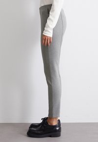 Pantaloni grigi a gamba affusolata realizzati in un tessuto morbido, dotati di una vita alta e dettagli di cucitura laterale, abbinati a scarpe nere con lacci.