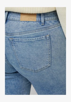 Hellblaue Jeans aus Denim mit Gesäßtasche und markenprägendem braunem Lederetikett von s.Oliver, kombiniert mit einem cremefarbenen Strickpullover.