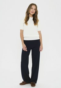 Fehér rövid ujjú blúz, amely bő szabású sötétkék nadrággal van párosítva. Az öltözet lazán illeszkedik, sima textúrájú, egyszerű dizájnelemekkel.