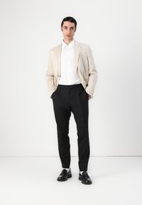 Beige linblazer over en hvit skjorte, kombinert med svarte bukser og svarte loafers. Viser en skreddersydd passform og glatte teksturer.