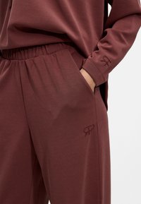 Bordo komplet za opuštanje s opuštenim gornjim dijelom s okruglim izrezom i hlačama s elastičnim pojasom, izrađen iz mekanog, glatkog materijala.