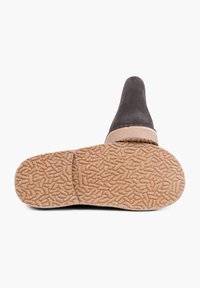Zapato de ante negro con un tacón bajo y una suela de goma color beige que presenta un patrón texturizado. El zapato tiene una puntera redondeada y una costura mínima visible.