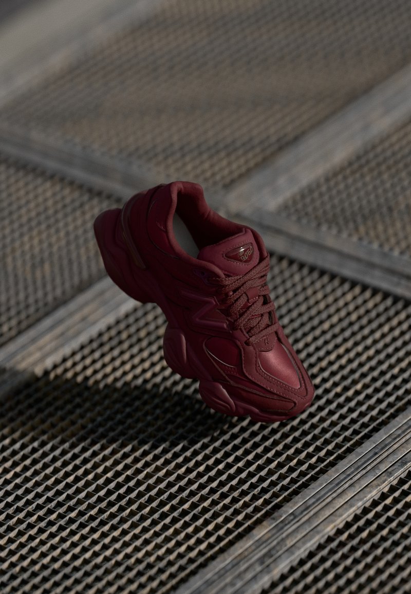 Bordeaux sneaker met een gestructureerde bovenkant, vetersluiting en opvallende contouren van de zool. Beschikt over een logo en naadloze accenten van synthetisch materiaal.