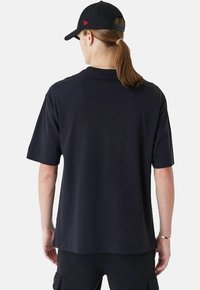 T-shirt nera in cotone con maniche corte e scollatura a girocollo, con una vestibilità rilassata e un design pulito e semplice. Indossata con un cappellino nero.