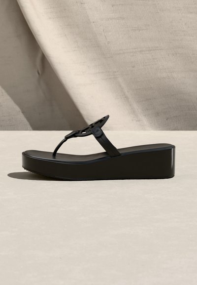 Μαύρο πλατφόρμα σανδάλι με χοντρή σόλα και ένα λεπτό λουράκι με δάχτυλο που διαθέτει ένα κυκλικό διακοσμητικό στοιχείο.