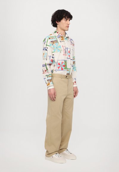 Button-up shirt with multicolored playful patterns on a white background, paired with beige wide-leg trousers and white sneakers.