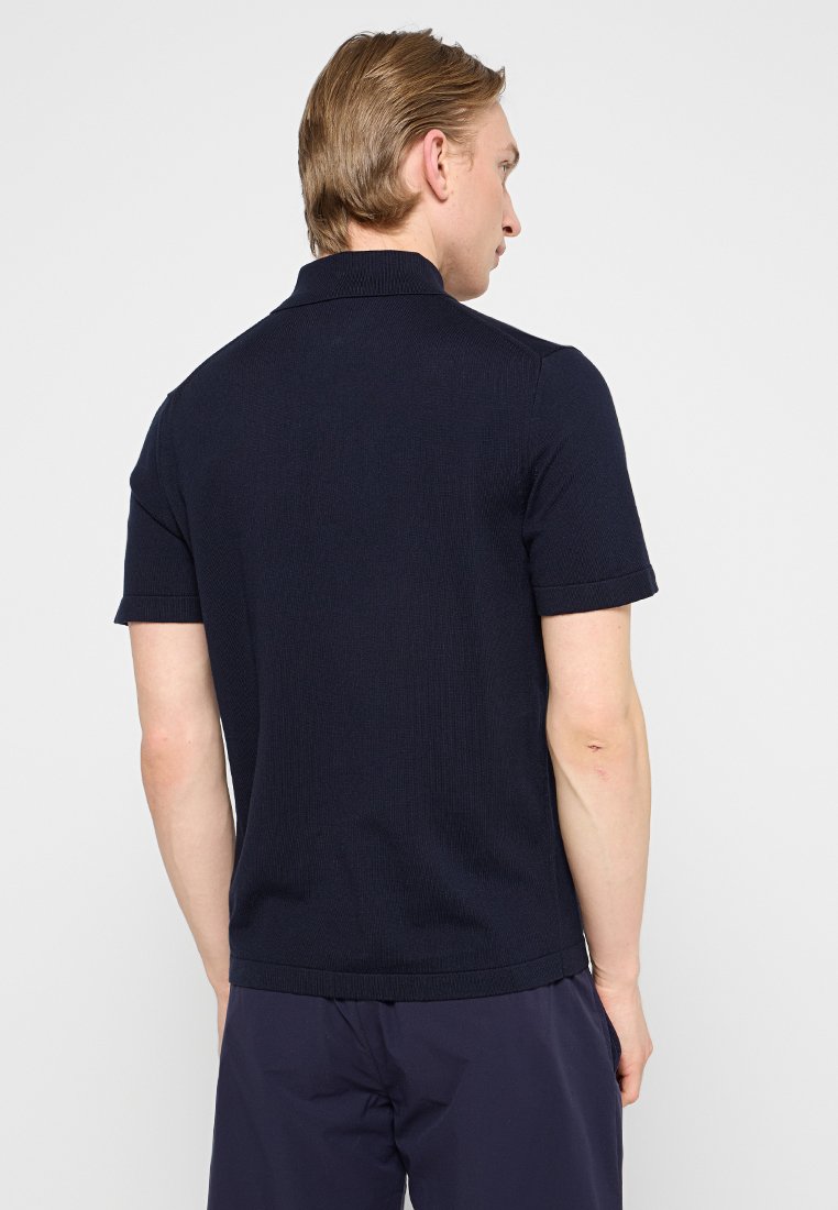 Granatowa koszulka polo z krótkim rękawem o rypsowej strukturze, z płaskim kołnierzykiem i podwiniętymi mankietami, z prostym dołem i bez widocznych logo.