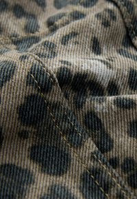 Denim tkanina s uzorkom leopard, vidljivim detaljima šivanja; mekana tekstura, miješanje nijansi smeđe, sive i crne boje.