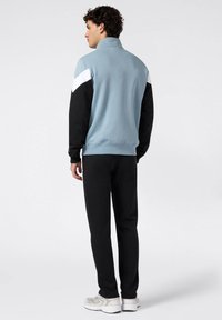 Sudadera azul claro con detalles en negro y blanco, cuello alto y puños acanalados, combinada con pantalones de chándal negros y zapatillas de color claro.
