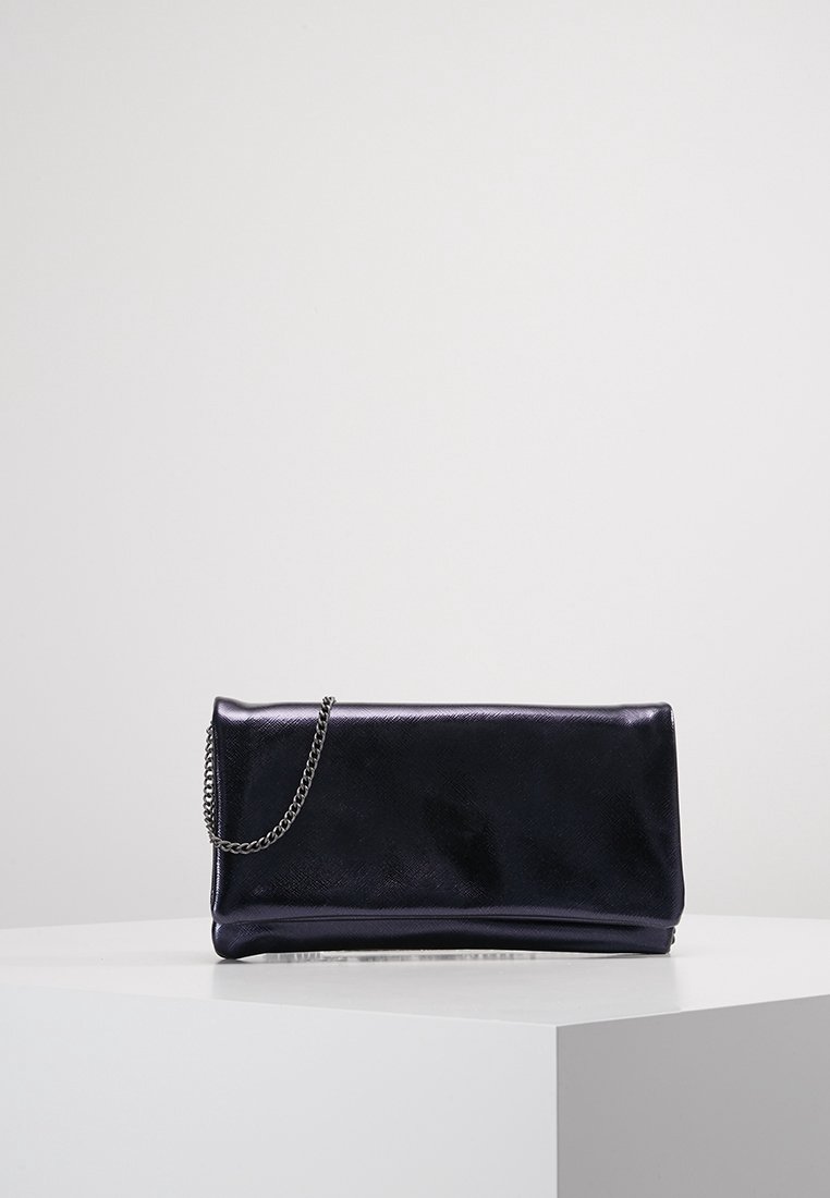 Pochette en cuir noir avec une chaîne argentée reposant sur un socle blanc sur un fond gris clair uni.