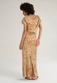 Abito beige con un motivo a griglia nei toni del marrone e dell'arancio. Presenta maniche corte, un collo drappeggiato e uno spacco laterale.