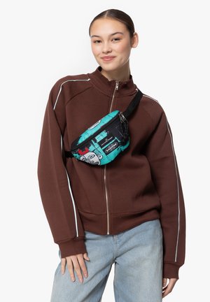 Fanny pack noir et turquoise avec un motif graphique, comportant une fermeture éclair et une sangle ajustable, porté sur un sweat à capuche marron zippé.
