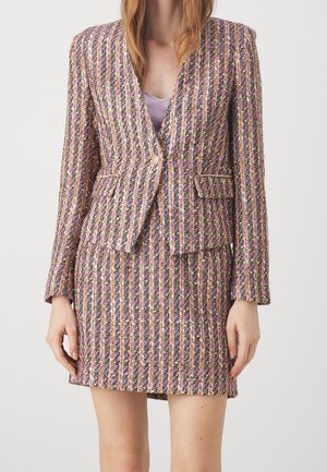 Mujer vistiendo un conjunto de blazer y falda de tweed texturizado y multicolor con rayas verticales y bolsillos con solapa, sobre una blusa lavanda.