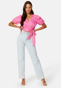 Top avvolgente rosa con maniche a palloncino, annodato in vita. Abbinato a jeans a vita alta blu chiaro e sandali con tacco trasparente.