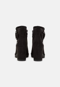 Botas negras de ante hasta el tobillo con un alto tacón cuadrado, cierre de cremallera lateral y detalle decorativo de hebilla en el lado exterior.