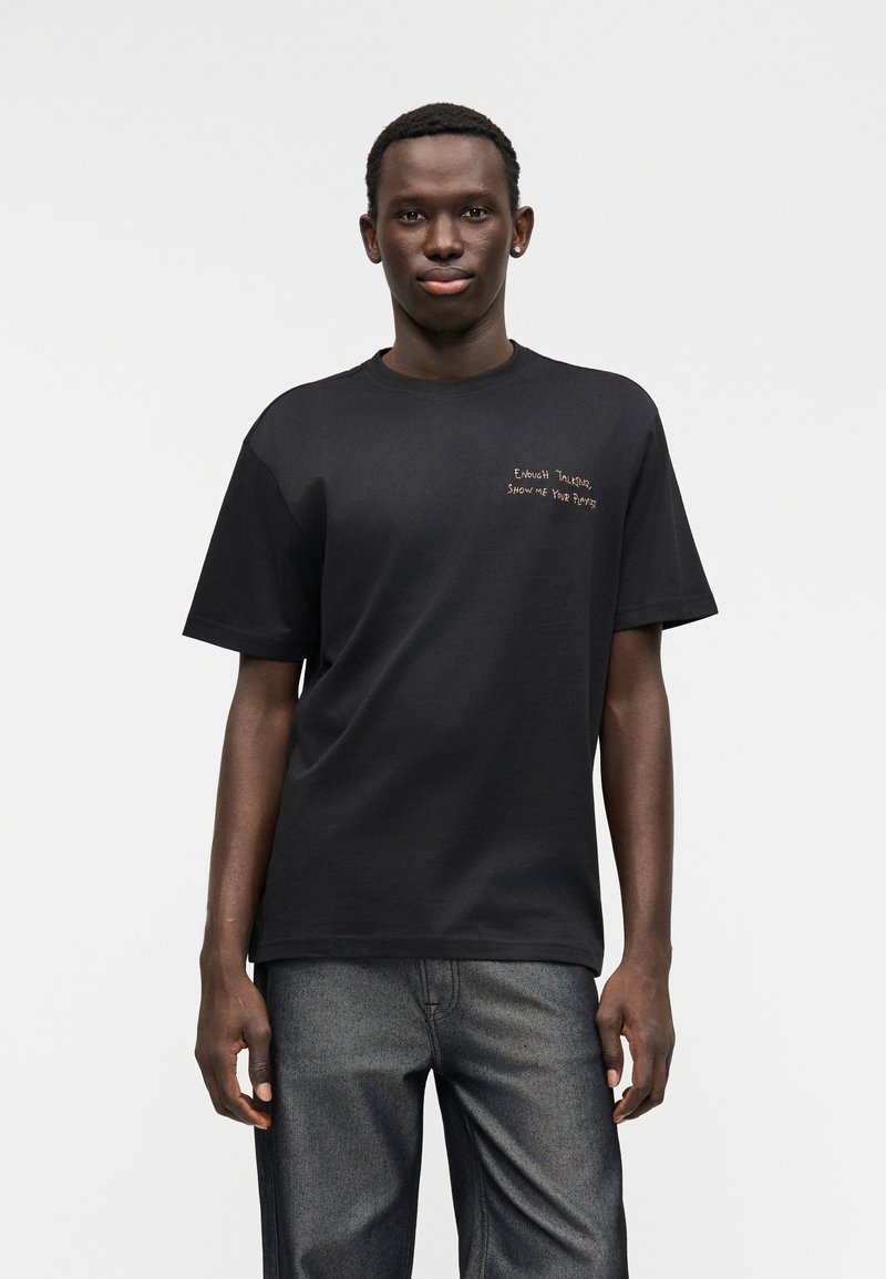 Μαύρο βαμβακερό μπλουζάκι με κοντά μανίκια και στρογγυλή λαιμόκοψη. Διαθέτει ανάγλυφη χρυσή κεντημένη φράση στο αριστερό στήθος.