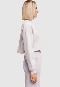 Šviesiai violetinė trumpa džemperio su aukštu kaklu ir nuolaidžiantys pečiais. Minkšta medžiaga su lygiu paviršiumi, derinama su tos pačios spalvos sportinėmis kelnėmis.