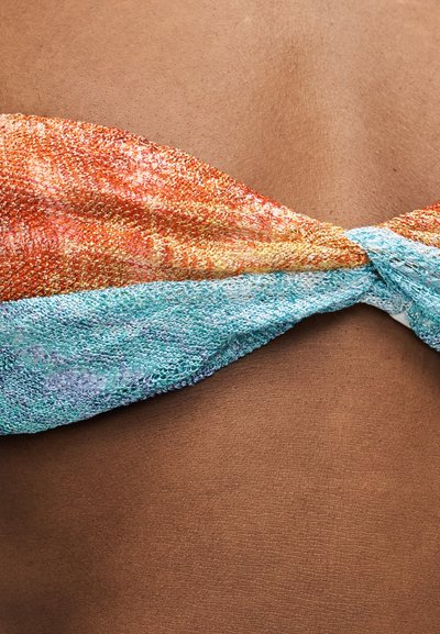 Gros plan sur le haut du dos d'une personne portant un haut de bikini en tricot multicolore avec des tons orange et bleu, noué au centre.