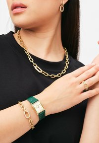 Gul kedja halsband, grön klocka med rektangulär urtavla och läderarmband, gul bracelet med länkade accenter, gul hoop örhängen och ring.