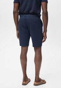 Mörkblå shorts med elastisk midja, bakfickor och rak passform. Tyget verkar lätt och mjukt. Bärs med sandaler.