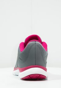 Zapatilla deportiva gris con una superficie texturizada, acentos en rosa y suela blanca. Presenta un collar acolchado y un diseño elegante y moderno.