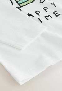 Fehér hosszú ujjú ing zöld és fekete grafikával. Puha pamut anyag, egyenes szabás és gondosan varrott szélek.