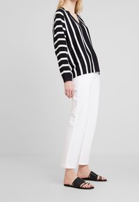 Black and white striped lightweight sweater with a V-neckline, paired with white wide-leg trousers and black slide sandals.