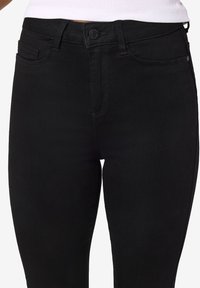 Črne jeans hlače s prilegajočim dizajnom, petimi žepi in gumbom za zapiranje. Gladka tekstura in minimalno šivanje, vidno vzdolž šivov.