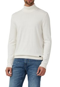 Weißer Strickpullover mit Rollkragen, Rippbündchen und Saum, aus weichem Material. Kombiniert mit blauen Denim-Jeans. Kleines Markenetikett am Saum.