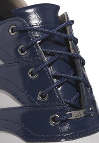 Námořnické modré syntetické boty s lakovaným povrchem, obsahující kovové očka, ploché námořnické tkaničky a bílou gumovou podrážku.